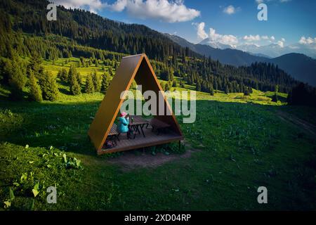 Touriste randonneur femme en veste bleue prendre un repos dans la maison d'été avec toit de triangle au drone aérien beau paysage de montagne sauvage et Fores d'épicéa Banque D'Images