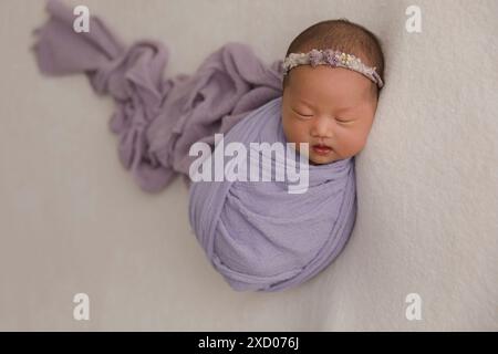 Vue de dessus d'un nouveau-né dormant sur un lit sous une couverture beige et une fleur de bandeau pliable sur sa tête. Copier l'espace. Concept de soins du nouveau-né. Banque D'Images