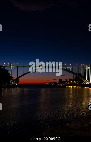 Pont Arrabida illuminé sur le fleuve Douro au crépuscule à Porto, Portugal. Les lumières de la ville se reflètent sur les eaux calmes ci-dessous, créant une scène pittoresque. Banque D'Images