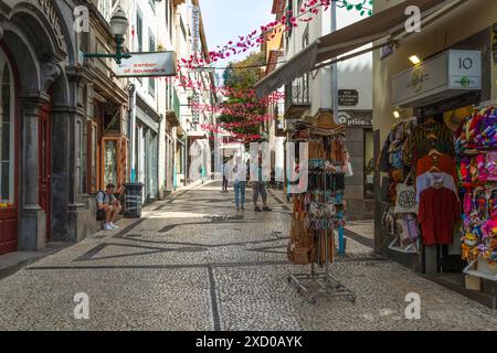 Les gens marchent à travers une rue commerçante étroite confortable dans le centre historique de Funchal. Banque D'Images