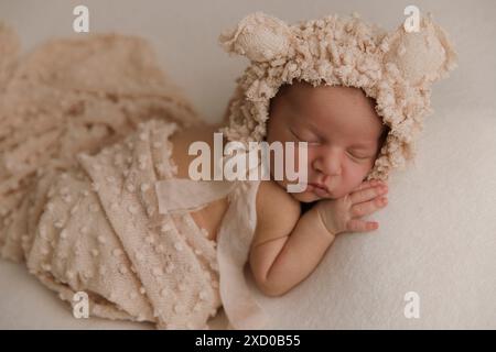 Vue de dessus d'un nouveau-né dormant sur un lit sous une couverture beige et une fleur de bandeau pliable sur sa tête. Copier l'espace. Concept de soins du nouveau-né. Banque D'Images