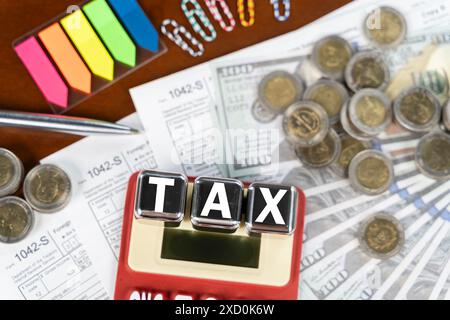 Une calculatrice rouge avec le mot taxe écrit dessus. Il y a aussi quelques pièces de monnaie et une pile de papier sur la table Banque D'Images