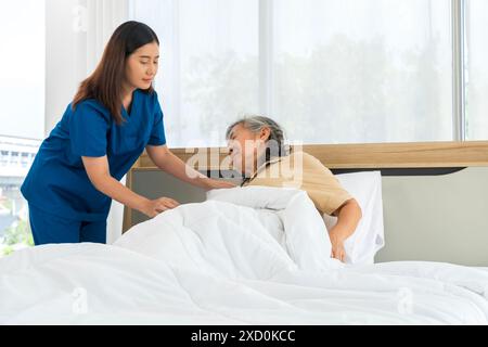 Une femme en uniforme bleu aide une femme âgée au lit. Concept d'infirmière assistante. Banque D'Images