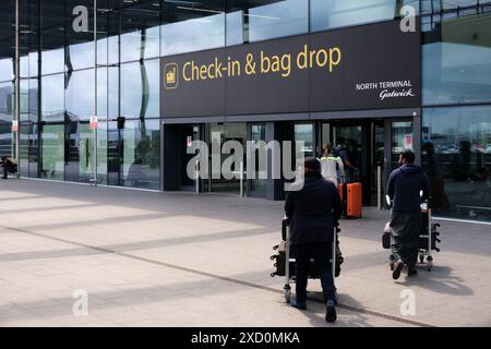 Aéroport de Gatwick, Royaume-Uni : 22 avril 2024. Les passagers transportant des chariots à bagages s'approchent de l'entrée du terminal sud pour s'enregistrer et déposer leurs bagages. Banque D'Images