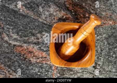 Une vue de dessus d'un mortier en bois et pilon placé sur une surface de pierre texturée. Idéal pour les concepts culinaires, de cuisine et de cuisine naturelle. Banque D'Images