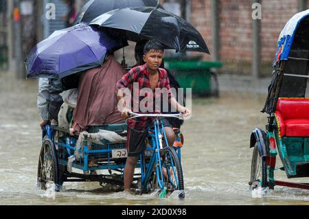 Sylhet, Bangladesh. 19 juin 2024. Sylhet, Bangladesh. Les résidents de la zone résidentielle d'élite de ​​Shahjal Upashahar de Sylhet se déplacent dans des pousse-pousse et des fourgonnettes de pousse-pousse sur des routes inondées. Alors que la situation des inondations s’aggrave dans la ville de Sylhet, de nombreuses personnes dans les zones résidentielles d’Upashahar quittent leurs maisons et déménagent vers des endroits plus sûrs. En raison des fortes pluies et des pentes montantes, des inondations ont eu lieu dans toutes les zones résidentielles le long des rives de la rivière de la ville de Sylhet. Crédit : majoritaire World CIC/Alamy Live News Banque D'Images