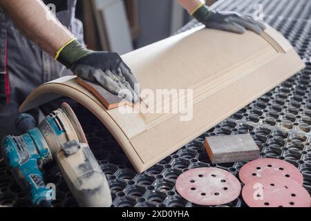 Un menuisier masculin sabre les façades de meubles en bois avec une ponceuse dans une usine de production de meubles, concept de traitement du bois Banque D'Images