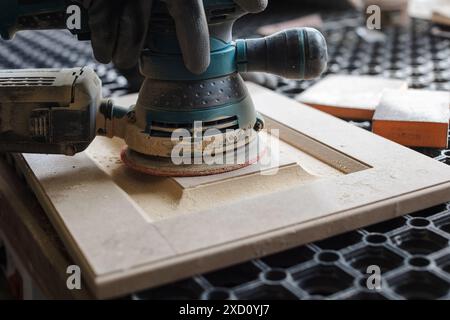 Un menuisier masculin sabre les façades de meubles en bois avec une ponceuse dans une usine de production de meubles, concept de traitement du bois Banque D'Images