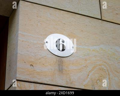 Numéro 6 sur un mur extérieur de maison. La plaque métallique est émaillée et de couleur blanche. Le design est très vintage et rétro. Le six fait partie d'une adresse Banque D'Images