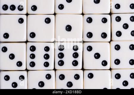 De nombreux dés avec des points noirs sur des surfaces blanches sont étroitement empilés, affichant différents nombres dans un arrangement rapproché Banque D'Images