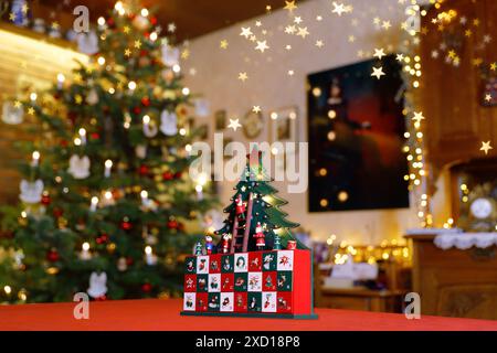 Calendrier de l'Avent peint en bois avec arbre de Noël stylisé, minuscules figures et tiroirs debout sur une table au milieu d'une décoration de Noël Banque D'Images