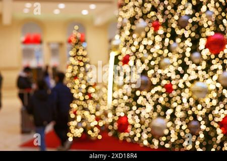 Vue floue de certains clients marchant le long de décorations d'arbre de Noël opulemment éclairées dans le centre commercial pendant la période de Noël Banque D'Images