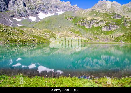 Un magnifique lac alpin avec une eau turquoise limpide reflétant les montagnes environnantes et un ciel bleu vif. Banque D'Images