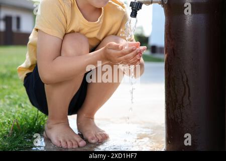 Rareté de l'eau. Petit garçon buvant de l'eau du robinet à l'extérieur, gros plan Banque D'Images