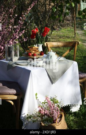 Beau bouquet de tulipes et gaufres fraîchement cuites sur table servi pour boire du thé dans le jardin Banque D'Images