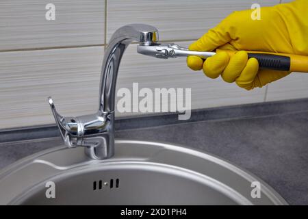 Un plombier en gants de caoutchouc jaunes dévisse l'aérateur de robinet avec une clé réglable Banque D'Images