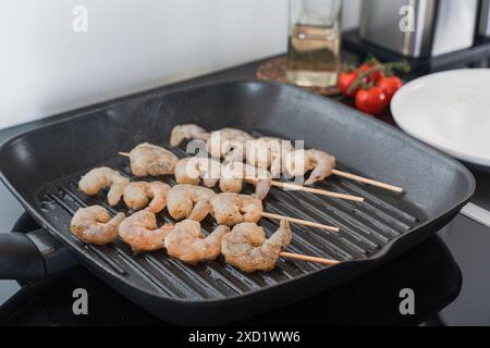 Brochettes de crevettes crues assaisonnées cuisant sur une poêle à griller dans la cuisine. Banque D'Images