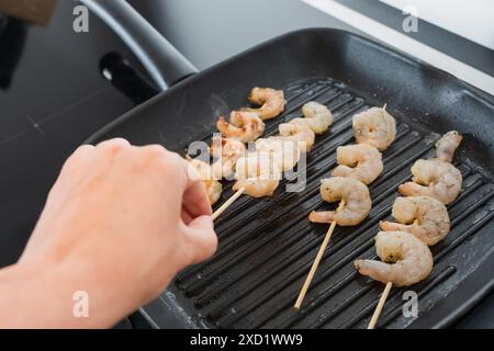 perte d'une main en tournant des brochettes de crevettes crues assaisonnées sur une poêle à griller, Banque D'Images