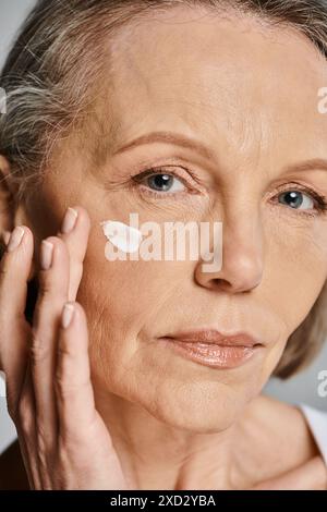 Une femme âgée élégante appliquant doucement de la crème sur son visage, en prenant soin de sa peau. Banque D'Images