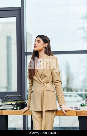 Une femme en costume bronzé se tient confiante devant un bureau. Banque D'Images