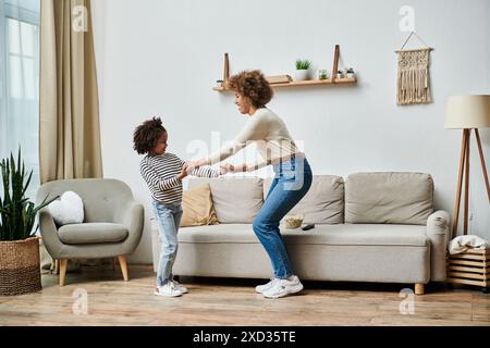 Une mère afro-américaine et sa fille dansent joyeusement sur un canapé dans leur salon, partageant un moment spécial ensemble. Banque D'Images