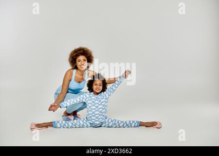 Une heureuse mère afro-américaine et sa fille en pyjama pratiquant le yoga ensemble sur un fond blanc. Banque D'Images