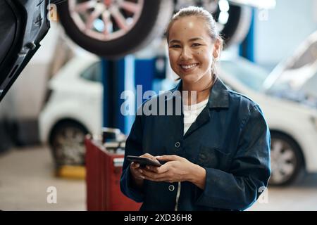 Portrait, mécanicien et femme avec smartphone dans un atelier de réparation automobile, sourire et internet pour le calendrier en ligne. Visage, inspection et personne avec téléphone portable Banque D'Images