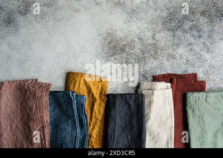 Vue de dessus de serviettes textiles colorées soigneusement disposées sur un fond en béton texturé, parfait pour un cadre de table moderne. Banque D'Images