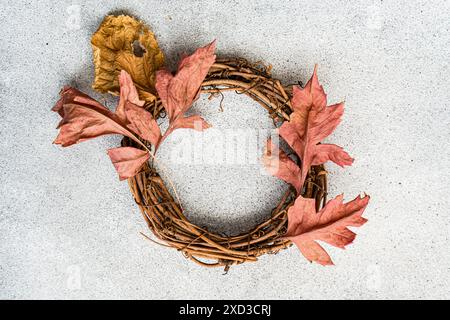 Une couronne automnale vibrante faite de branches torsadées et ornée de feuilles orange, située sur un fond gris texturé Banque D'Images