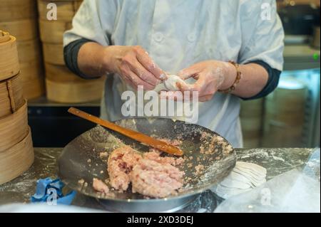 Gros plan sur les mains d'un chef méconnaissable qui confectionne des boulettes maison remplies de viande, avec des cuiseurs vapeur en bambou en arrière-plan. Banque D'Images
