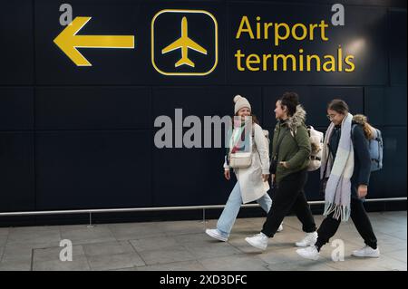 Un trio de femmes voyageant avec des sacs à dos passe devant un panneau indiquant les terminaux de l'aéroport. Banque D'Images