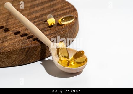 Une image en gros plan montre des capsules oméga 3 dorées sur une cuillère en bois, reposant sur une planche à découper rustique texturée dans un éclairage lumineux Banque D'Images