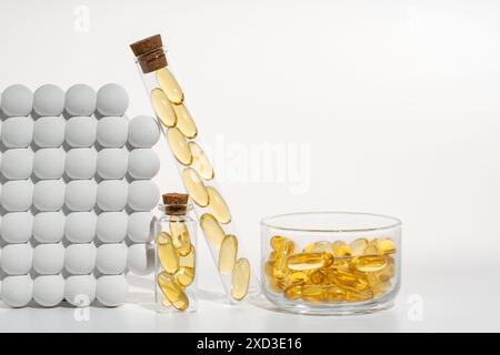 Un arrangement artistique de capsules d'huile de poisson oméga 3 présentées dans divers récipients en verre, y compris un flacon verseur et un bol, serrés contre un b blanc Banque D'Images