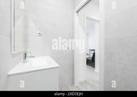 Salle de bains moderne et élégante dans un style minimaliste, avec un lavabo mural blanc avec un grand meuble de toilette gris clair et un aperçu du lit attenant Banque D'Images