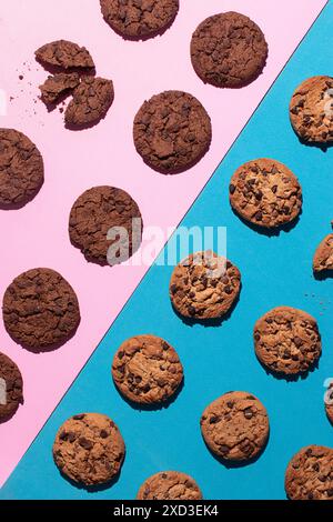 Une photographie à plat représentant un assortiment de pépites de chocolat et de biscuits au chocolat doubles disposés sur un double fond rose et bleu. Un cooki Banque D'Images