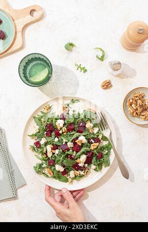 Une salade de roquette magnifiquement arrangée avec du fromage de chèvre, des noix et de la betterave sur une assiette en céramique beige. La lumière naturelle améliore les couleurs éclatantes et t Banque D'Images