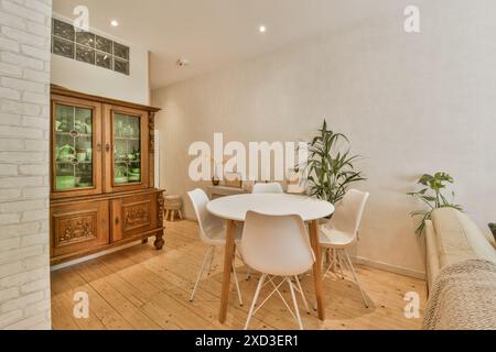 Salle à manger confortable avec une table blanche, des chaises modernes et une armoire en bois classique, complétée par des plantes d'intérieur pour une ambiance fraîche Banque D'Images