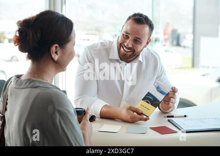 Vendeur, femme et brochure à la concession automobile avec discussion, promotion ou rabais avec sourire dans le bureau. Personnes, brochure et heureux pour le client Banque D'Images