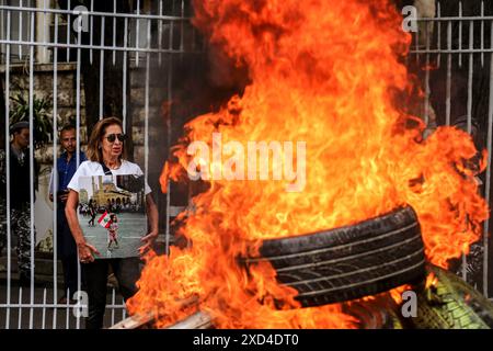 20 juin 2024, Beyrouth, Liban : une parente d'Alexandra Najjar, une jeune libanaise de 3 ans, qui a perdu la vie dans l'explosion massive du port de Beyrouth le 5 août 2020, porte sa photo près des flammes de pneus en feu au palais judiciaire de Beyrouth lors d'une manifestation des familles des victimes de l'explosion. Moins de deux mois avant le 4ème anniversaire de l'explosion qui a tué plus de 200 personnes, presque tout reste inconnu de qui a ordonné l'expédition à pourquoi les autorités ont ignoré les avertissements répétés du danger. Les familles des victimes ont insisté pour obtenir des réponses, accusant les partis politiques d'obstruction Banque D'Images