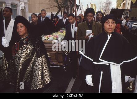 Mount Sion Spiritual Baptist Church, l'évêque George Gifford Noel de Grenade était mort, les membres de la communauté de l'église suivent en procession alors que le cercueil est roulé dans la rue jusqu'au cimetière de Kensal Green. Mère Twila Noel (à gauche) dirige le cortège funéraire. Kensal Green, Londres, Angleterre des années 1994 1990 Royaume-Uni HOMER SYKES Banque D'Images