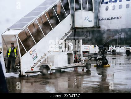 Francfort, Allemagne - 4 mai 2019 : un membre de l'équipage au sol de l'aéroport se tient près d'un escalier d'embarquement de passagers attaché à un Airbus A321-200 par temps de pluie, avec des gouttes de pluie visibles sur la fenêtre Banque D'Images