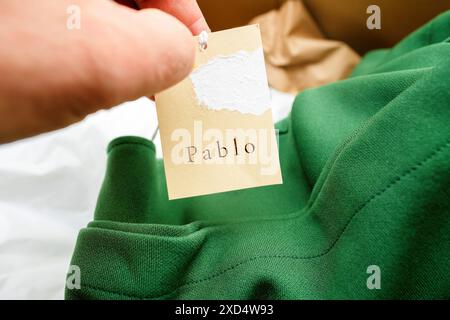 Paris, France - 28 mars 2024 : une main masculine tenant une nouvelle étiquette de vêtements de mode Pablo avec le logo, placée sur un fond de vêtement et de carton, mettant l'accent sur la marque et le style de la mode rapide Banque D'Images