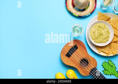 Chapeau sombrero mexicain, ukulélé, tequila, chips de nachos, guacamole et maracas sur fond bleu clair, plat. Espace pour le texte Banque D'Images