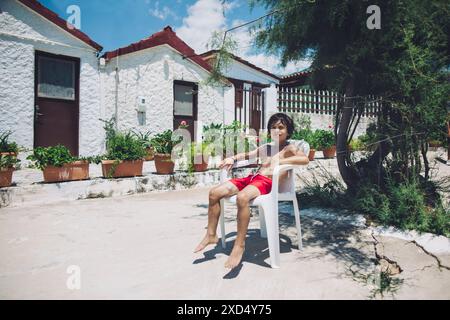 Garçon se détend sur une chaise de patio à l'extérieur des maisons blanchies à la chaux en grèce Banque D'Images