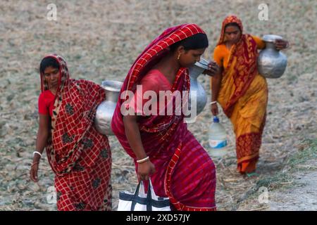 20 juin 2024, Dhaka, Dhaka, BANGLADESH : des femmes bangladaises transportent de l'eau potable après l'avoir récupérée d'une source d'eau douce, marchant un long chemin pour recueillir de l'eau potable dans la zone côtière de Khulna, au Bangladesh. Selon une étude de l’American Geophysical Union, l’élévation du niveau de la mer, qui affecte la disponibilité de l’eau potable, entraînera la migration d’environ 1,3 millions de personnes à travers le pays d’ici 2050. Une combinaison d'inondations dues aux marées, d'inondations dues aux ondes de tempête et d'intrusion d'eau salée entraîne une augmentation de la salinité dans les eaux souterraines et les eaux douces Banque D'Images