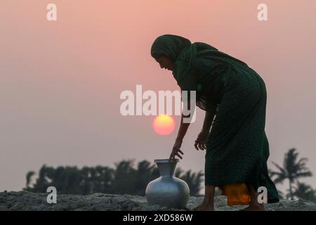 20 juin 2024, Dhaka, Dhaka, BANGLADESH : une femme bangladaise transportant de l’eau potable après l’avoir récupérée d’une source d’eau douce, marchant un long chemin pour récupérer de l’eau potable dans la zone côtière de Khulna, au Bangladesh. Selon une étude de l’American Geophysical Union, l’élévation du niveau de la mer, qui affecte la disponibilité de l’eau potable, entraînera la migration d’environ 1,3 millions de personnes à travers le pays d’ici 2050. Une combinaison d'inondations dues aux marées, d'inondations dues aux ondes de tempête et d'intrusion d'eau salée entraîne une augmentation de la salinité dans les eaux souterraines et les étangs d'eau douce Banque D'Images