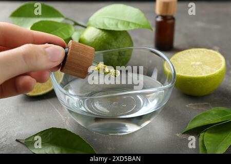 Femme goutte à goutte d'huile essentielle de la pipette dans le bol à la table grise, gros plan Banque D'Images