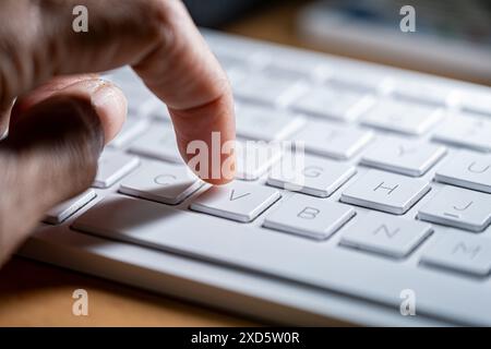 Gros plan du doigt d'une personne appuyant sur la touche 'V' d'un clavier d'ordinateur blanc. Banque D'Images