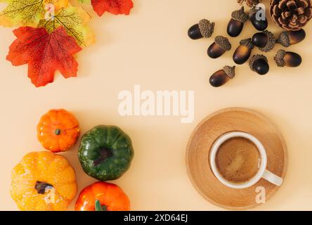 Scène d'automne ou d'automne faite avec une tasse de café, des feuilles d'automne colorées, diverses citrouilles, pommes de pin et noix avec espace de copie sur fond beige pastel. Banque D'Images