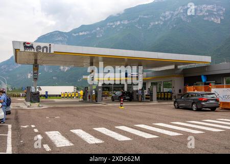 Véhicules se ravitaillant dans une station-service ENI sur l'autoroute A22 au Sudtirol, avec des montagnes majestueuses en arrière-plan sous un ciel nuageux. Banque D'Images